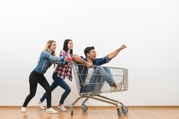 The three friends fun with a shopping cart on a white wall background