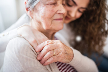 A teenage girl with grandmother at home, hugging.