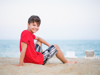 Wall Mural - Teen boy on sand on beach - summer vacation, close-up portrait. Child looking up at camera.