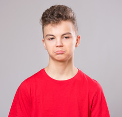 Wall Mural - Emotional portrait of caucasian upset problem teen boy. Sad boy looking at camera. Worried  child wearing red t-shirt, on gray background.