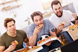 © Kalim - Happy male friends eating pizza and watching tv