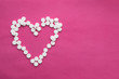 heart of white pills on a pink background