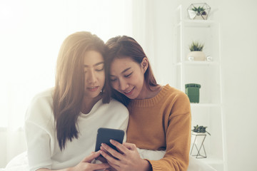 Wall Mural - Beautiful young asian women LGBT lesbian happy couple sitting on bed hug and using phone together bedroom at home. LGBT lesbian couple together indoors concept. Spending nice time at home.