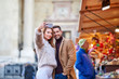 © Spectral-Design - A beautiful young couple taking a selfie with christmas market in the background.