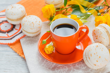 Wall Mural - Orange cup of black coffee, yellow roses flowers and sweet pastel french macaroons