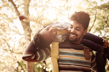 Wall Mural - Happy African American father in park carrying his daughter on shoulders.