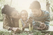© Mladen - Happy African American parents in park with daughter using mobile phone together.