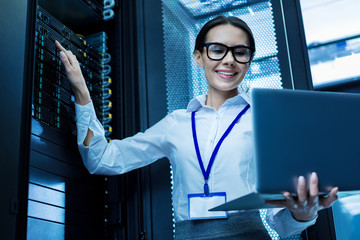 My best day. Content attractive woman working in a server cabinet and holding her laptop