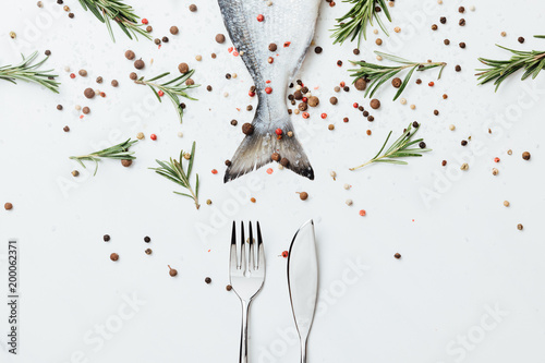 Fotografía Raw fish with cutlery and rosemary with pepper isolated on white
