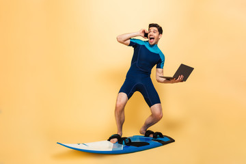 Excited young man on surfing board talking by phone using laptop computer.