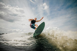 Athletic man wakesurfing on the board against the cloudy sky
