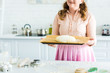 © LIGHTFIELD STUDIOS - cropped image of woman holding tray with dough for baking bread in kitchen