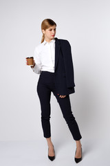 girl in full growth in a business suit and a white shirt is holding a glass of coffee on a white background