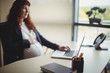 © Wavebreak Media - Pregnant businesswoman touching her belly while using laptop
