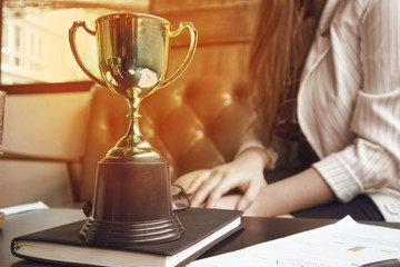 Wall Mural - glow trophy on working table which have document and pen and black book and bakcground working women