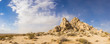 Sand desert holds pile of rock boulders forming a hill in the midst of the Mojave desert.