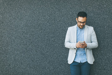 Young businessman with mobile phone by the grey wall