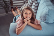 © Fxquadro - Portrait of a happy little girl with long brown hair and charming smile, looking at a camera, lying on a sofa at home