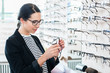© Kzenon - Woman taking glasses off shelf to try in optician shop