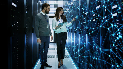 female and male it engineers discussing technical details in a working data center/ server room with