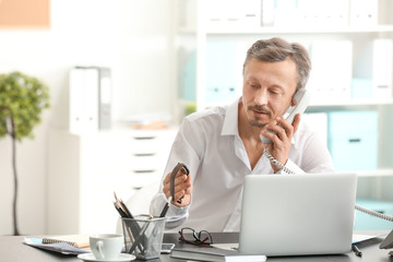 Canvas Print - Mature man talking on phone while working indoors