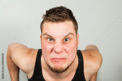 Fotografia, Obraz Young funny bearded guy dressed in black tank top sitting on the toilet on gray background