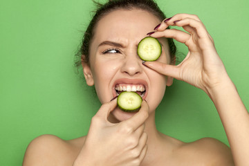 Frowning young woman biting slice of cucumber on green background