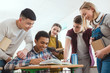 © LIGHTFIELD STUDIOS - smiling african american schoolboy writing in notebook while his classmates standing around