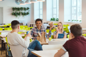 happy multiethnic group of high school students chatting while taking lunch at school cafeteria