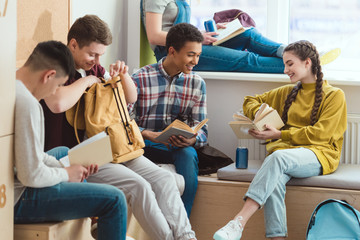 Smiling multicultural high school pupils reading books and talking during school break