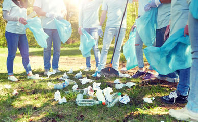 Poster - volunteering, charity, people and ecology concept - group of volunteers with garbage bags and rake cleaning area in park