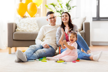 Wall Mural - family, holidays and people concept - happy mother, father and little daughter clapping hands at home