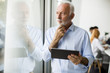 © BGStock72 - Senior businessman standing by window with digital tablet in his hand