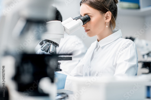 Fotomural Young female medic in uniform working with microscope making analysis at the lab