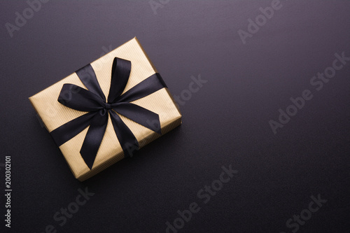 Fotografía Hands holding wrapped gift box with colored ribbon as a present for Christmas, new year, mother's day, anniversary, birthday, party, on black background, top view