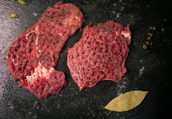 Raw pork chop with spices on a dark background.