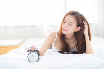 Wall Mural - Beautiful asian young woman turn off alarm clock in morning, wake up for sleep with alarm clock, relax and lifestyle concept.