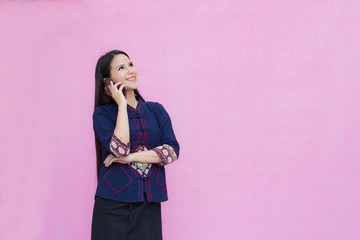 Portrait of asian young girl in traditional thai dress and holding smartphone  isolated on pink background. Cotton dress