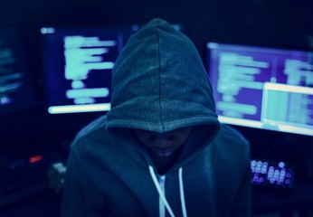 Wall Mural - Hacker wearing a hoody with computers in the background