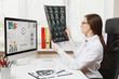 © ViDi Studio - Female doctor sitting at desk with computer, film x-ray the brain by radiographic image ct scan mri in light office in hospital. Woman in medical gown in consulting room. Healthcare, medicine concept.
