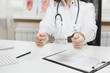 © ViDi Studio - Close up arrested female doctor sitting at desk with medical documents in light office in hospital. Woman in medical gown, stethoscope, hands with handcuffs in consulting room. Medicine, law concept.