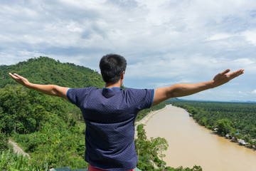 young man happy and show to strength with hands rise up on beautiful river Landscape with beautiful cloudy sky