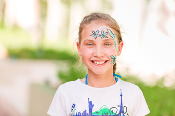 Happy little girl with face art paint in the park.