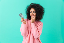 Portrait Of Charming American Woman 20s With Afro Hairstyle Holding Plastic Credit Card With Pleasure, Isolated Over Blue Background