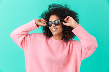 Poster - Fashion portrait of stylish woman 20s with afro hairstyle smiling and wearing black modern sunglasses, isolated over blue background