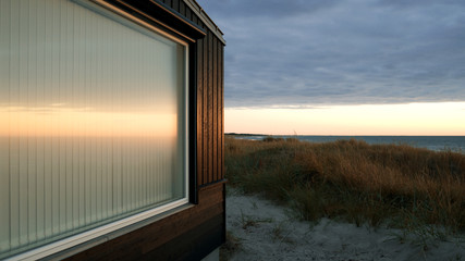 Laesoe / Denmark: The evening sun reflects in the window of a modern holiday house in the dunes in Vesteroe Havn