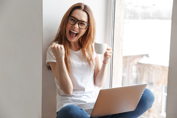 Poster - Cheerful woman in t-shirt and eyeglasses sitting on windowsill