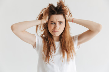 Wall Mural - Confused woman in t-shirt holding hair and looking at camera