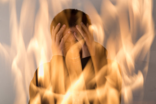 Fototapete - Double exposure. Man expressing his despair by holding his head in hands, and with fire background.