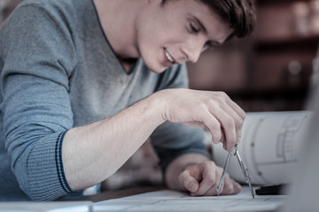 Wall Mural - Everything under control. Charming pleasant male engineer using compasses while creating blueprint and leaning above table